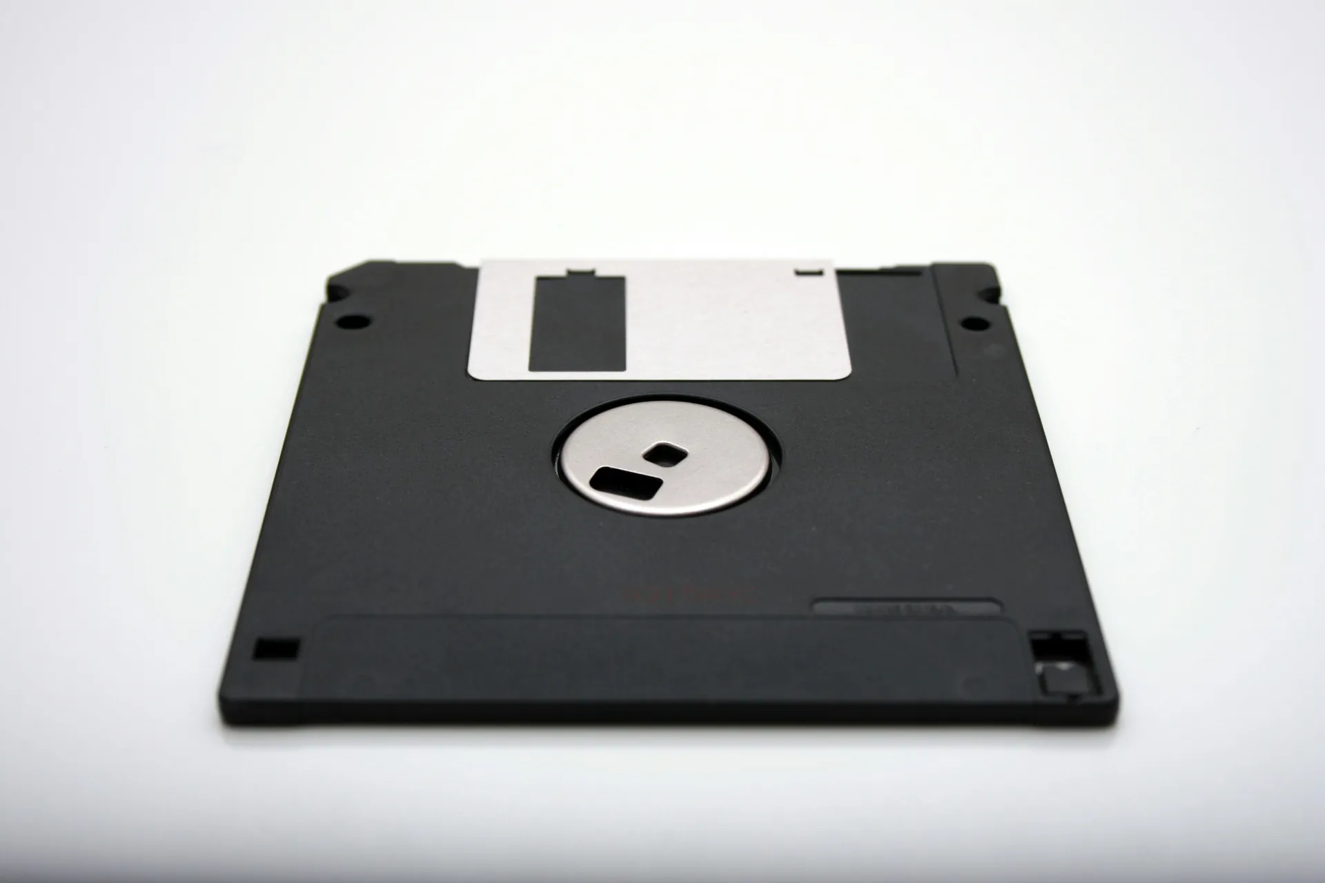 Vue rapprochée d’une disquette noire sur fond blanc, symbole emblématique du stockage informatique des années 80 et 90.
