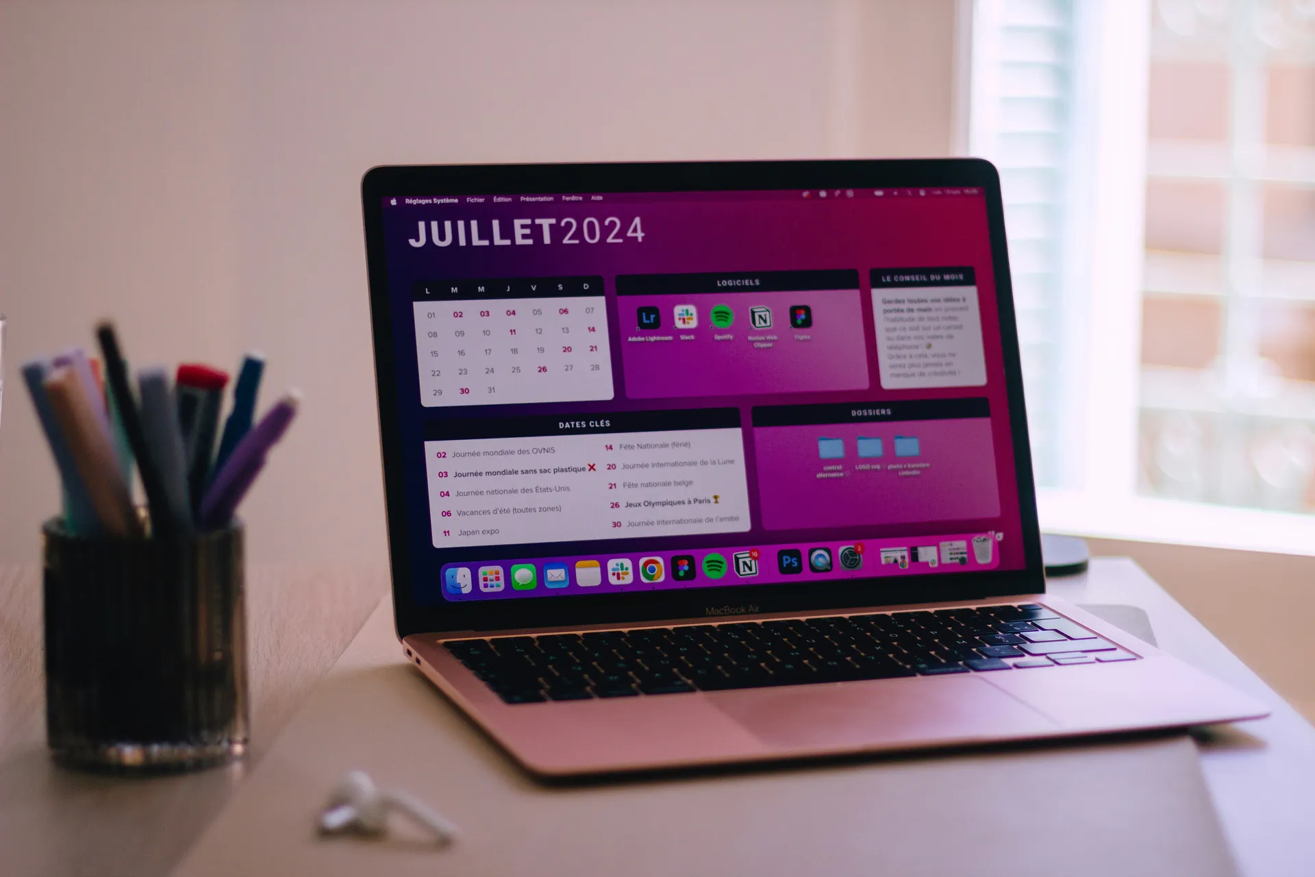 Laptop on a desk showing a monthly calendar planner next to a cup of pens