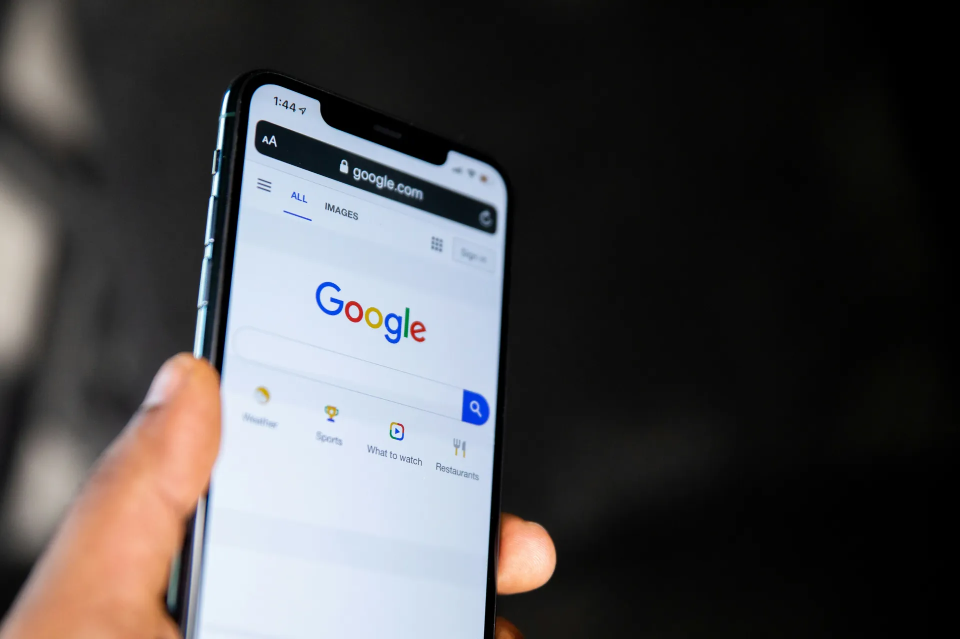 Écran d’un smartphone affichant la page d’accueil de Google, tenu dans une main, avec l’interface du moteur de recherche en premier plan.