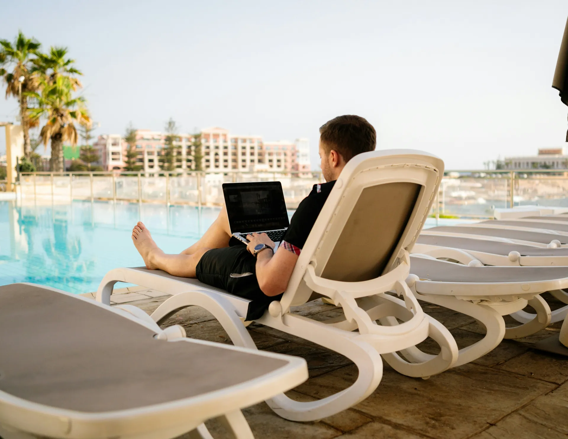 Monsieur sur son ordinateur au bord d'une piscine 