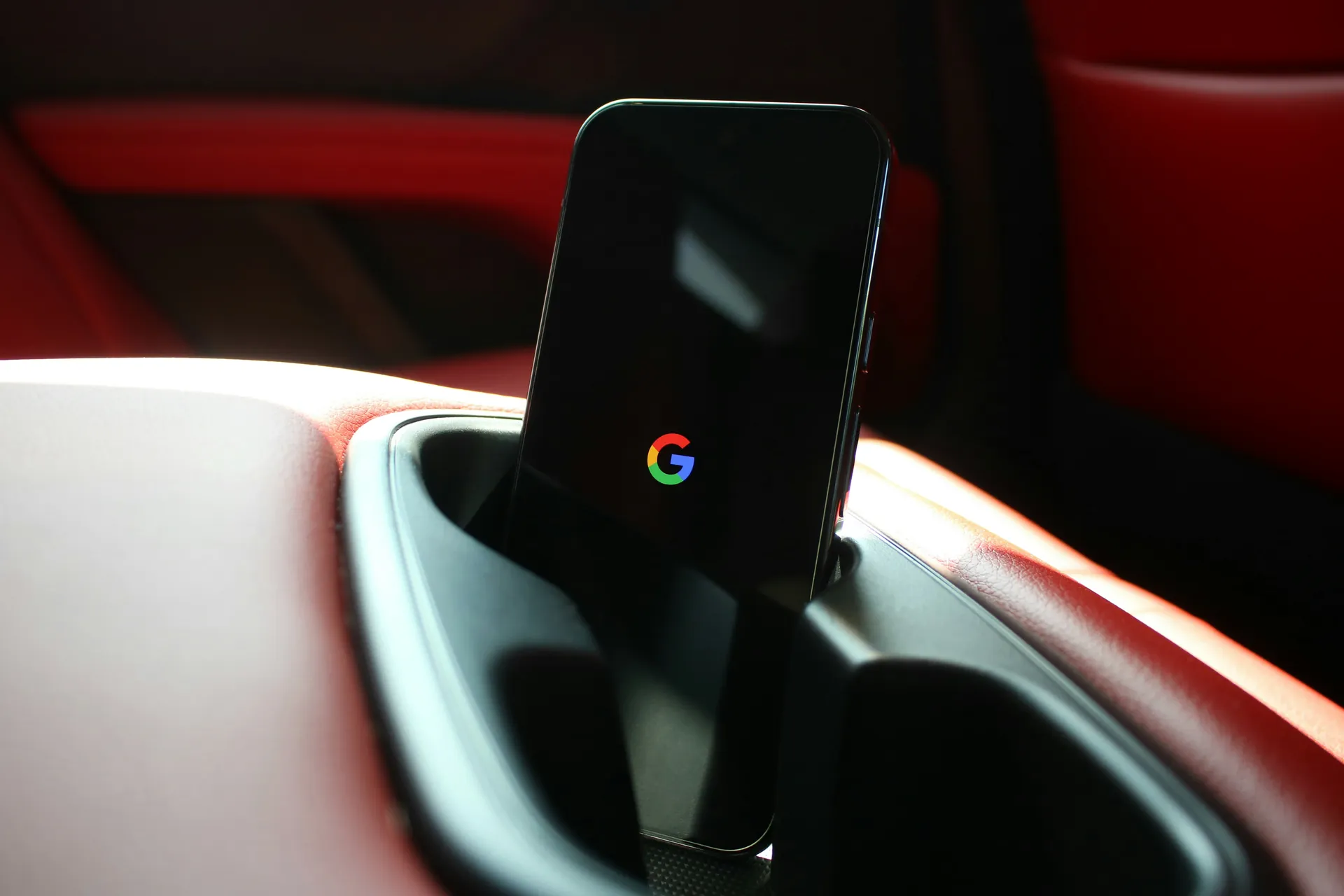 Smartphone posé dans un support de voiture avec un écran noir affichant le logo coloré de Google au centre.