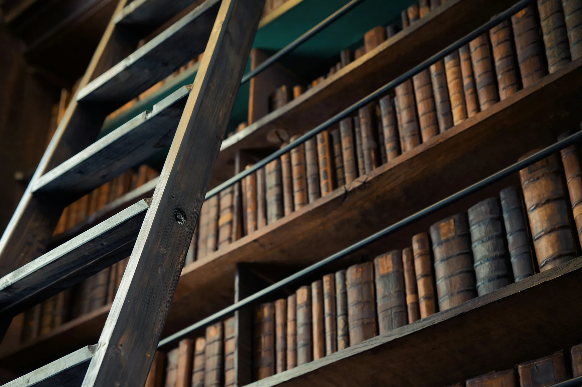 Bibliothèque ancienne en bois remplie de livres reliés, vue à travers une échelle en bois foncé